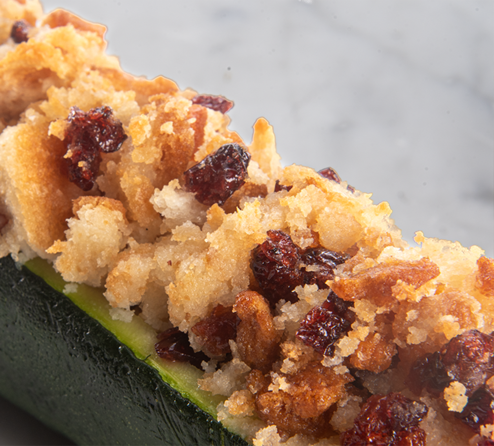 Plain stuffing cubes on green zucchini half, close-up of crumbly bread pieces